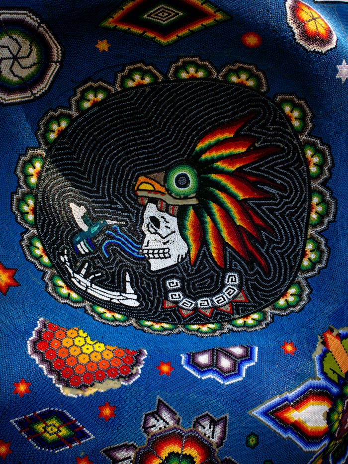 Vibrant Huichol beaded art tapestry featuring a skull with feather headdress.